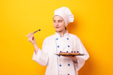 Lezzetli eklerlerle ve turuncu arka planda yaban mersinli üniformalı bir şekerci.