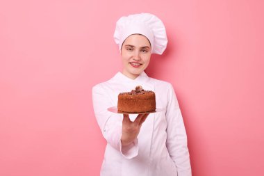 Üniformalı pastacı pembe arka planda lezzetli çikolatalı pasta tutuyor.