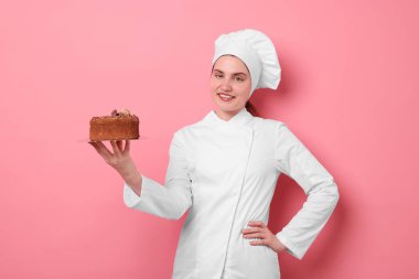 Üniformalı pastacı pembe arka planda lezzetli çikolatalı pasta tutuyor.