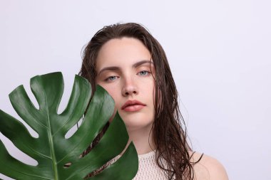 Gri arkaplanda doğal ten rengi ve canavar yaprağı olan güzel bir kadının portresi.