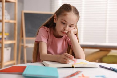 Disleksi. İçerideki masada kitap okuyan üzgün küçük kız.