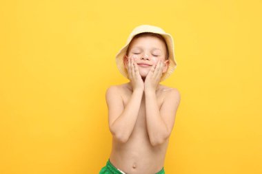 Küçük çocuk sarı arka planda cildine güneş kremi sürüyor.