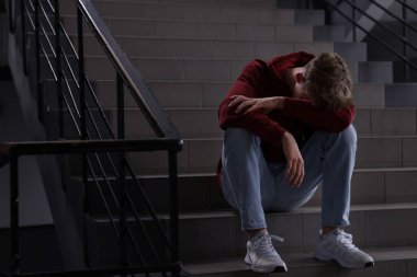 Zorbalık. Kapalı alandaki merdivenlerdeki üzgün genç çocuk. Metin için boşluk