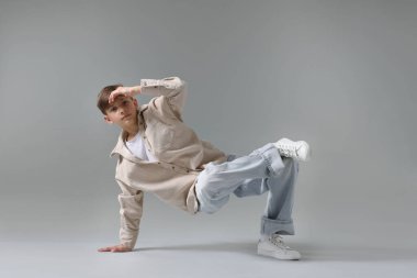 Açık gri arka planda dans eden şık elbiseli bir çocuk.