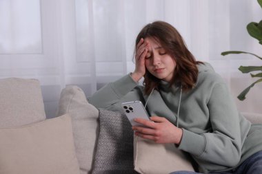 Siber zorbalık. Evdeki kanepede akıllı telefonlu üzgün bir genç kız. Metin için boşluk