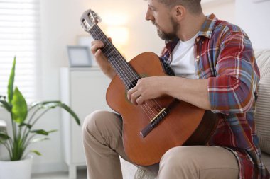 Evdeki kanepede gitar çalan adam.