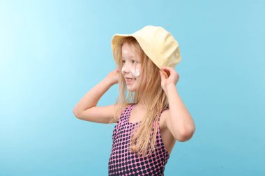 Yüzünde güneş kremiyle gülümseyen küçük kız açık mavi arka planda.