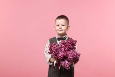 Pembe arka planda bir buket leylak çiçekli küçük çocuk.