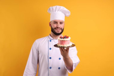 Üniformalı mutlu pastacı elinde turuncu arka planda böğürtlen tutuyor.