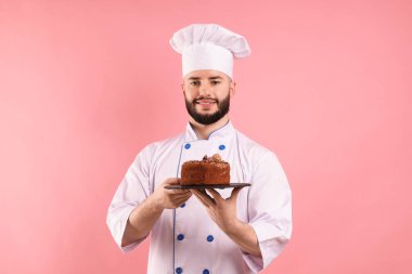 Üniformalı mutlu pastacı pembe arka planda çikolatalı pasta tutuyor