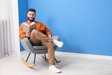 Kitapla evde sallanan koltukta rahatlayan gülümseyen adam. Metin için boşluk