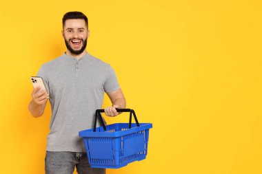 Boş alışveriş sepeti ve turuncu arka planda akıllı telefonu olan adam, mesaj için boşluk