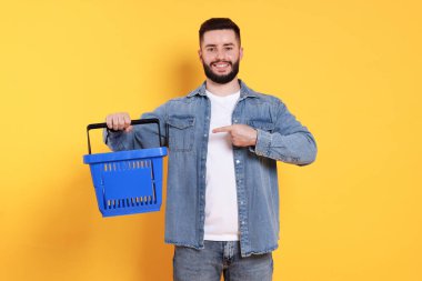 Turuncu arka planda boş alışveriş sepeti olan adam.