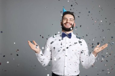 Doğum günün kutlu olsun. Gri arka planda konfeti yağmuru altında parti şapkası takan yakışıklı adam, mesaj için yer var.
