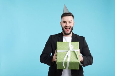 Doğum günün kutlu olsun. Açık mavi arka planda parti şapkası ve hediye kutusu olan yakışıklı bir adam.