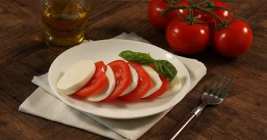 Kadın, ahşap masada domatesli ve fesleğenli mozzarellaya yağ döküyor.