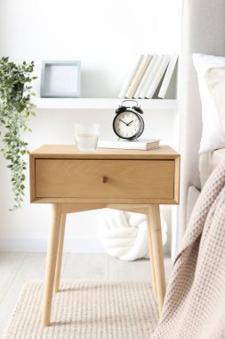 Alarmlı komodinli komodin, bir bardak su ve yatağın yanında kitap.