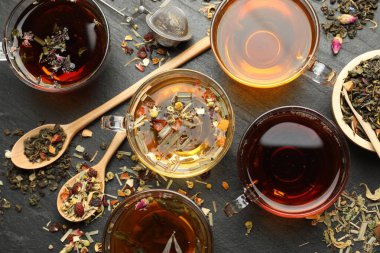 Farklı bitkisel çaylar ve kuru yapraklar siyah masada, düz yerde.