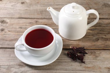 Lezzetli amber çayı fincanda, çaydanlık ve kuru roselle sepals ahşap masada