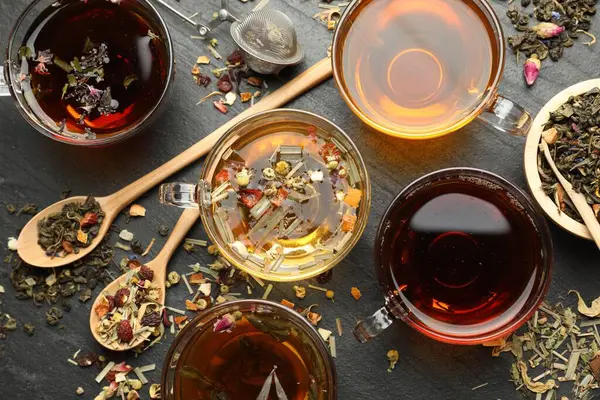 Farklı bitkisel çaylar ve kuru yapraklar siyah masada, düz yerde.