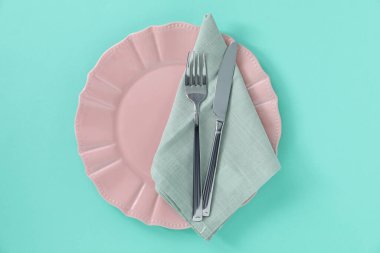 Turkuaz arka planda tabak, peçete ve çatal bıçak takımı, üst görünüm