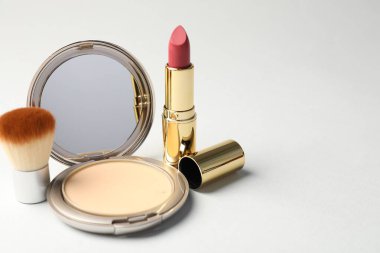 Açık gri arka planda ayna, fırça ve ruj ile yüz pudrası, yakın plan. Metin için boşluk