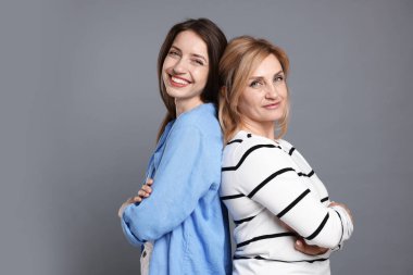 Neşeli anne ve kızı arka arkaya gri arka planda