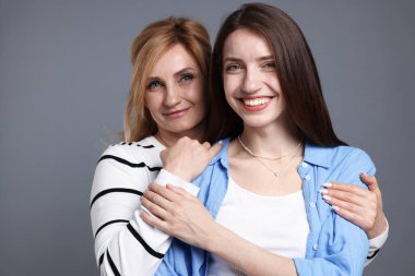 Anne ve kızı gri arka planda sarılıyorlar.