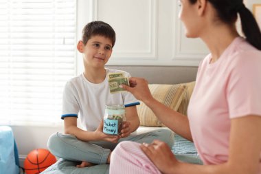 Anne ve oğul cep harçlığını evde kavanoza koyuyorlar, yakın plan.