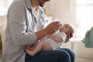 Babası evdeki kanepede bebeğini biberonla besliyor.