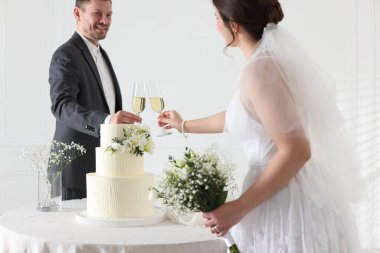 Mutlu evli çiftler masada kadeh tokuşturuyor. Düğün pastası içeride, seçici bir odak noktası var.