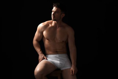 Siyah arka planda beyaz iç çamaşırlı genç bir adam.