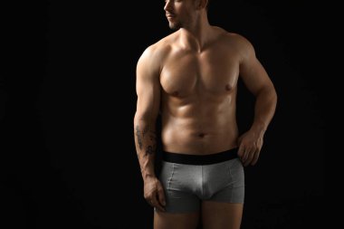 Siyah arka planda açık gri iç çamaşırlı genç adam, yakın plan.