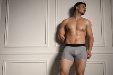 Beyaz duvarın yanındaki açık gri iç çamaşırlı genç adam. Metin için boşluk