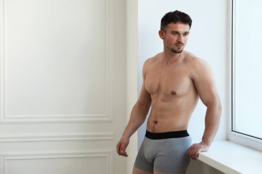 Beyaz duvarın yanındaki açık gri iç çamaşırlı genç adam. Metin için boşluk