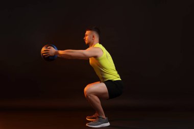 Siyah arka planda ilaç topuyla egzersiz yapan adam.