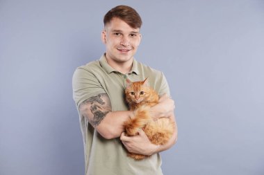 Gri arka planda kızıl kedisi olan sevimli bir adam.