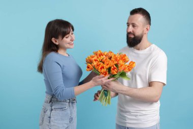 Bir adam açık mavi arka planda sevgili karısına güzel laleler sunuyor.