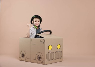 Bej arka planda kartondan yapılmış araba kullanırken boynuz izleri gösteren küçük bir çocuk. Metin için boşluk