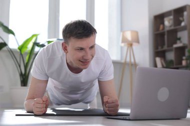 Evde bilgisayarla yoga dersi alan bir adam.