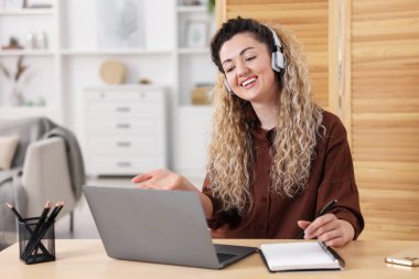 Kulaklıklı gülümseyen kadın, ofisteki masada dizüstü bilgisayar başında videokaset takıyor.