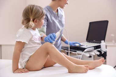 Sonograf, klinikte küçük kızın dizinin ultrason muayenesini yapıyor.