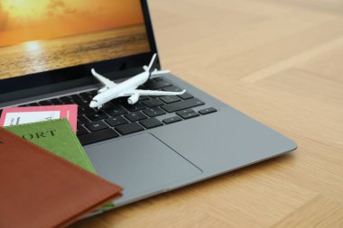 Pasaportlar, uçuş bileti, uçak modeli ve laptop ahşap masada, yakın plan.