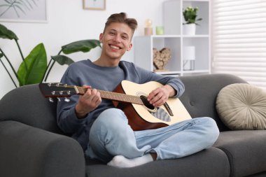 Mutlu adam içeride kanepede gitar çalıyor.