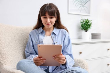 Evdeki koltukta modern tablet kullanan bir kadın.