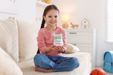 Evdeki kanepede bir kavanoz harçlığı olan kız.