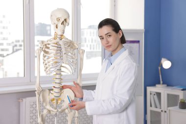 Doktor klinikteki insan iskeleti modelini işaret ediyor.