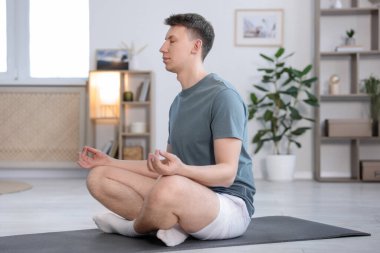 Genç adam evde yoga yapıyor.