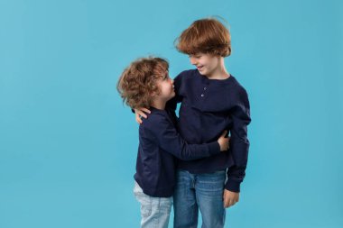 Sevimli küçük kardeşler açık mavi arka planda sarılıyorlar.