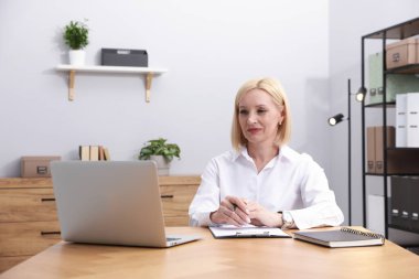 Ofiste dizüstü bilgisayarla çalışırken not alan profesyonel bir psikolog.